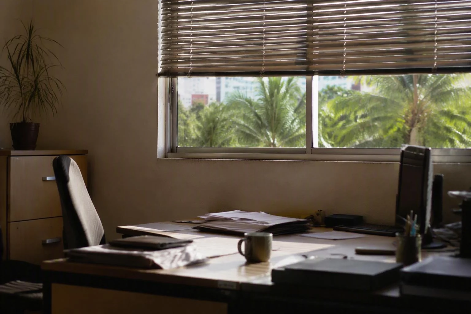 Janela de escritório com persiana meio aberta sobre a mesa de trabalho